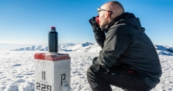 Rast auf einer Bergwanderung, ein Mann trinkt heißen Tee und blickt auf eine verschneite Berglandschaft