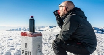 Rast auf dem Gipfel Rast auf einer Bergwanderung, ein Mann trinkt heißen Tee und blickt auf eine verschneite Berglandschaft